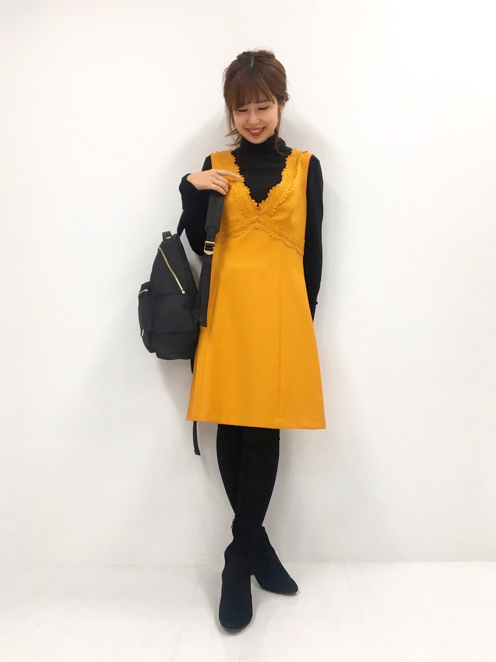 イエロー系のジャンパースカート、ブラック系のブーツ、ブラック系のニット/セーターを着用したレディースの秋コーディネートの1枚目の写真