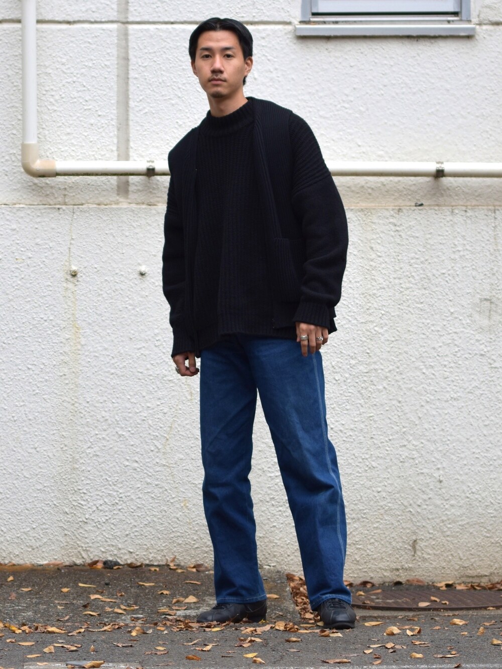 ブラック系のスニーカー、ブルー系のデニムパンツ、ブラック系のニット/セーターを着用したメンズの秋コーディネートの1枚目の写真