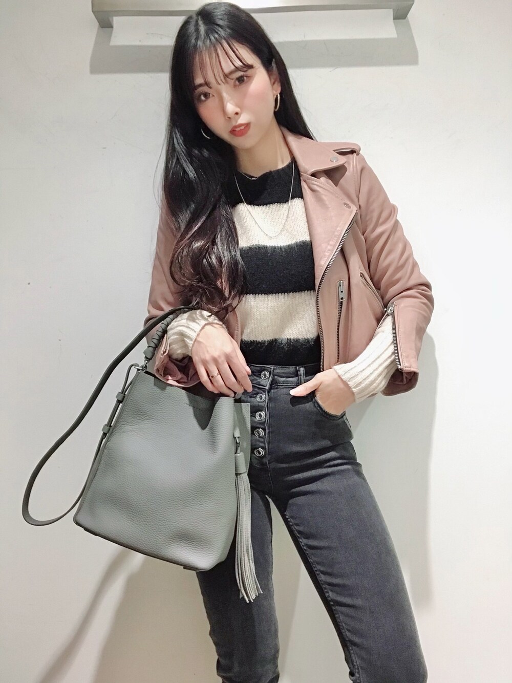 ピンク系のライダースジャケット、ブラック系のニット/セーター、ブラック系のデニムパンツを着用したレディースの冬コーディネートの1枚目の写真