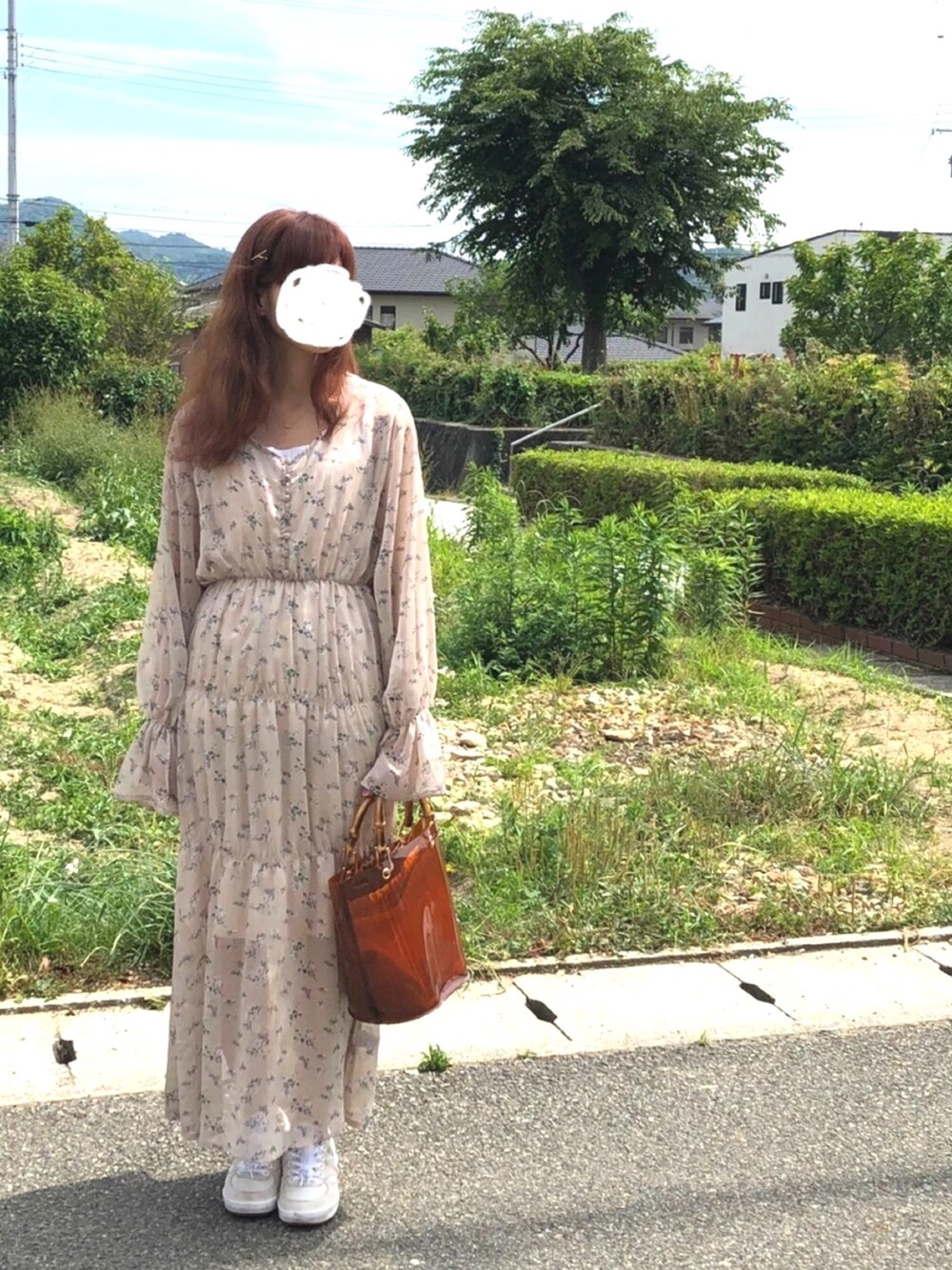 ベージュ系のワンピース、ブラウン系のハンドバッグ、ホワイト系のスニーカーを着用したレディースの夏コーディネートの1枚目の写真