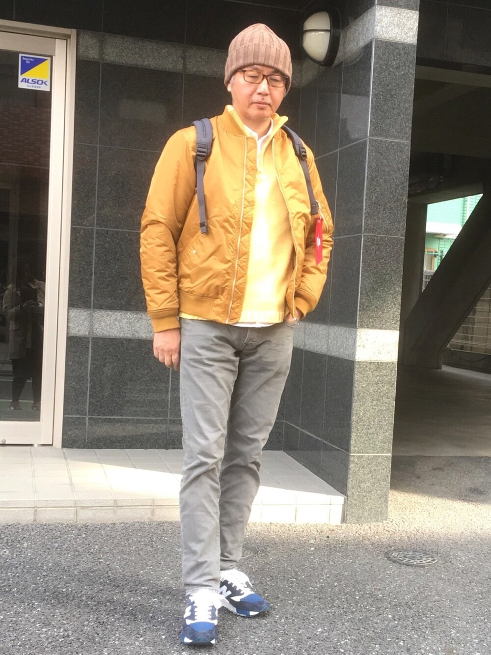 グレー系のデニムパンツ、ブルー系のスニーカー、ゴールド系のミリタリージャケットを着用したメンズの春コーディネートの1枚目の写真