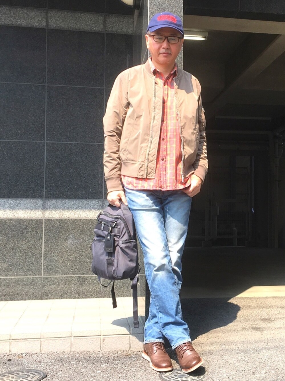 ブルー系のデニムパンツ、ブラウン系のブーツ、グレー系のバックパック/リュックを着用したメンズの春コーディネートの1枚目の写真