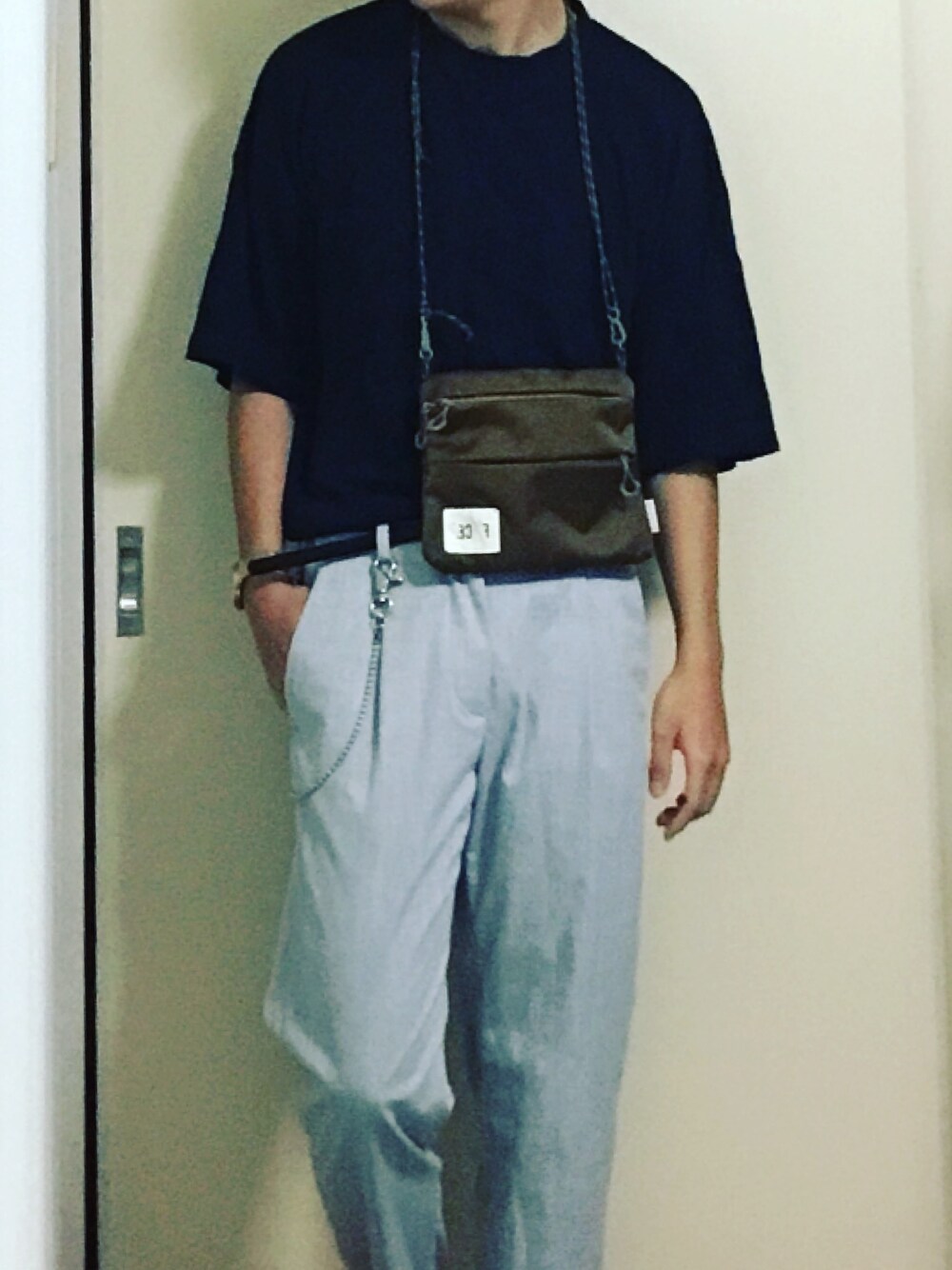 ブルー系のトップス、ベージュ系のショルダーバッグ、グレー系のスラックスを着用したメンズの夏コーディネートの1枚目の写真