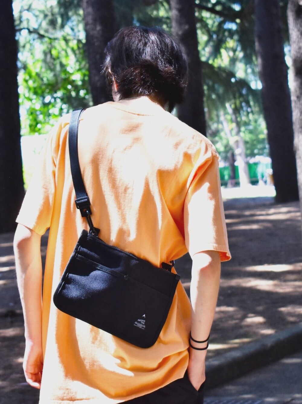 オレンジ系のTシャツ/カットソー、ブラック系のショルダーバッグを着用したメンズの夏コーディネートの1枚目の写真