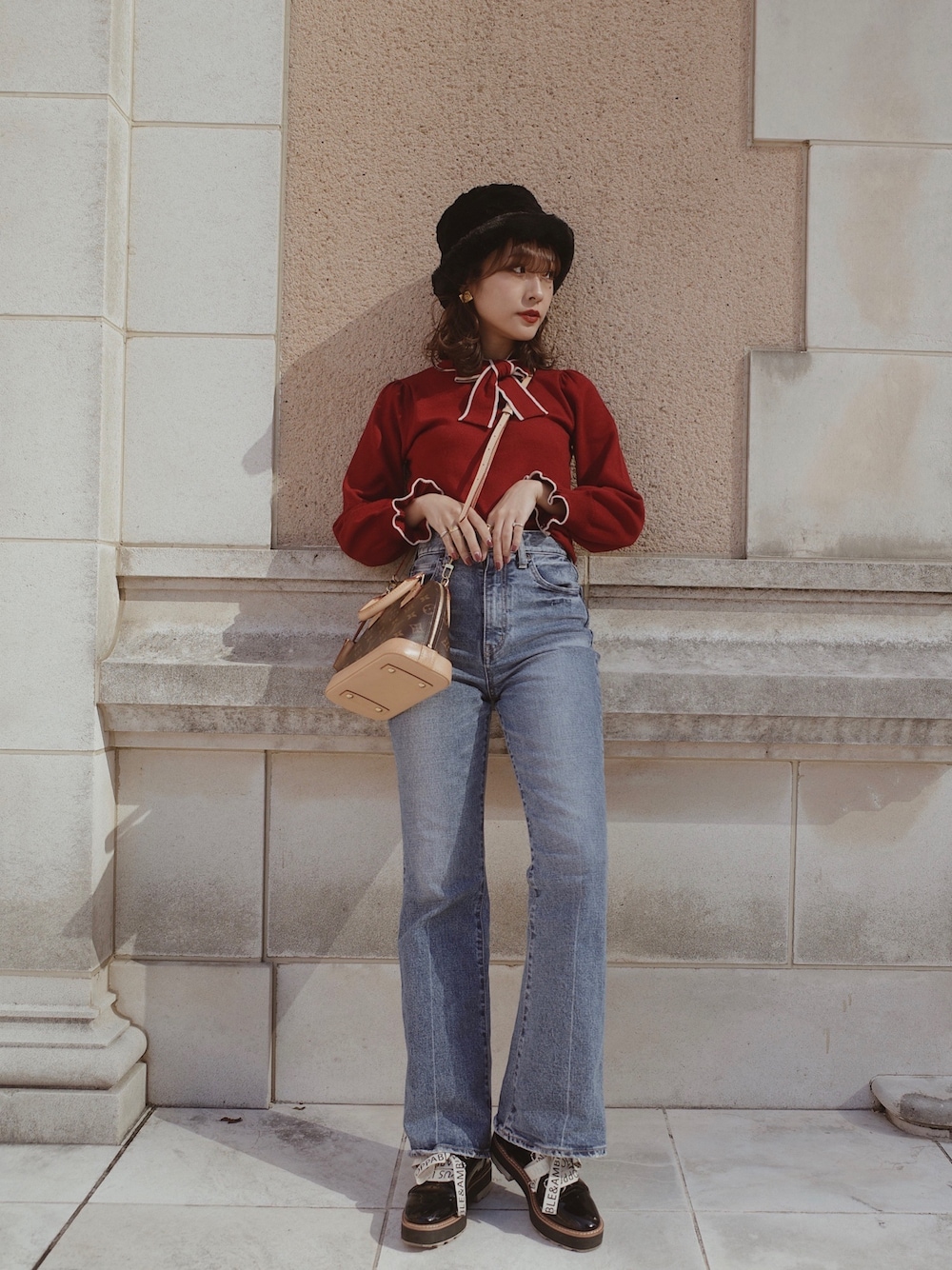 レッド系のニット/セーター、ブルー系のデニムパンツ、ブラウン系のバッグを着用したレディースの秋コーディネートの1枚目の写真