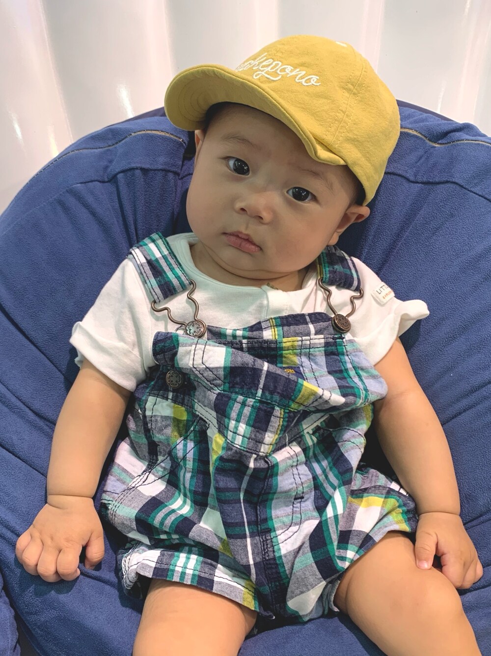 イエロー系のキャップ、グリーン系のロンパースを着用したキッズの秋コーディネートの1枚目の写真