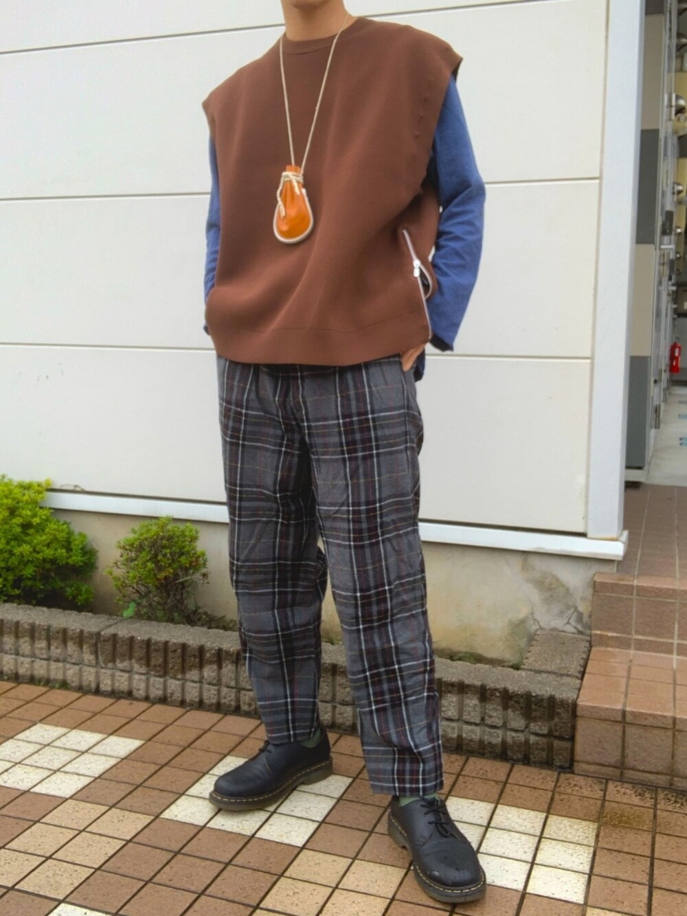 グレー系のスラックス、ブラック系のブーツ、ブラウン系のベストを着用したメンズの秋コーディネートの1枚目の写真