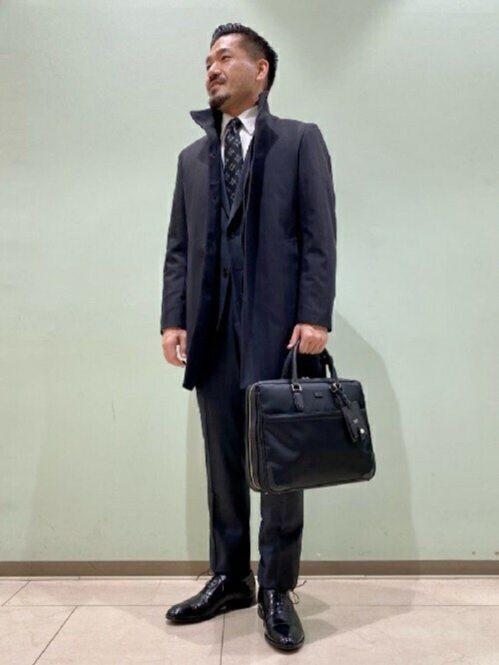 「コート、ビジネスバッグ、スーツ、ドレスシューズ、タケオキクチ(TAKEO KIKUCHI)、スタンドカラー、TAKEO KIKUCHI」｜「TAKEO KIKUCHIのダウンライナー付き メランジ ヘリンボン コート（その他アウター、ブラック系）」を使った、TAKEO KIKUCHIさん（メンズ・175cm）の冬コーディネートの1枚目の写真