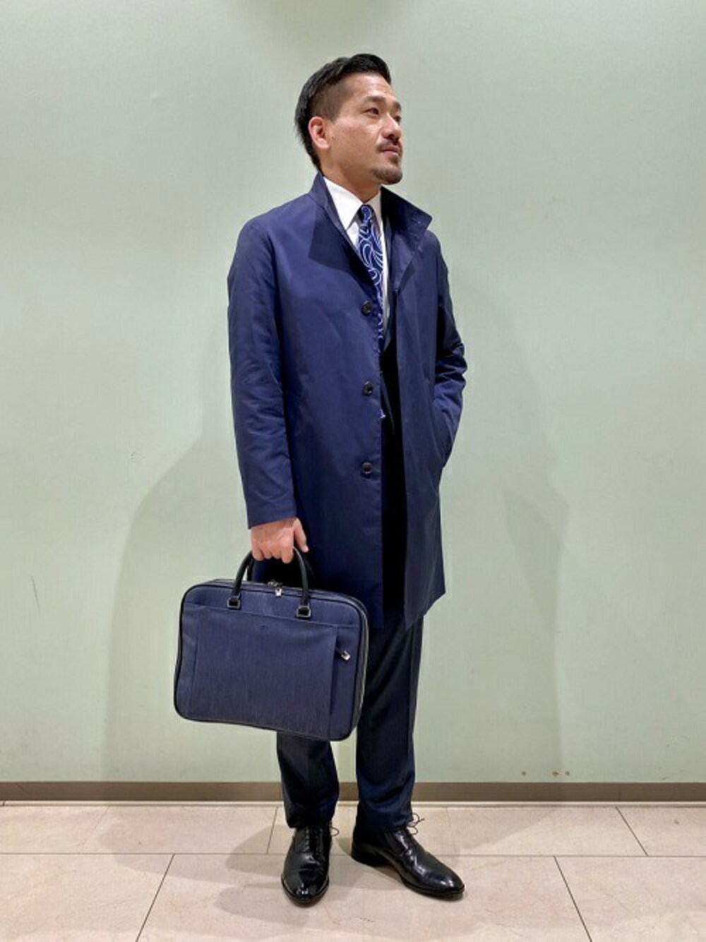 「コート、ビジネスバッグ、スーツ、ドレスシューズ、ネクタイ、タケオキクチ(TAKEO KIKUCHI)、スタンドカラー、スプリングコート、TAKEO KIKUCHI」｜「TAKEO KIKUCHIの耐久撥水 スタンドカラー コート（その他アウター、ブルー系）」を使った、TAKEO KIKUCHIさん（メンズ・175cm）の冬コーディネートの1枚目の写真