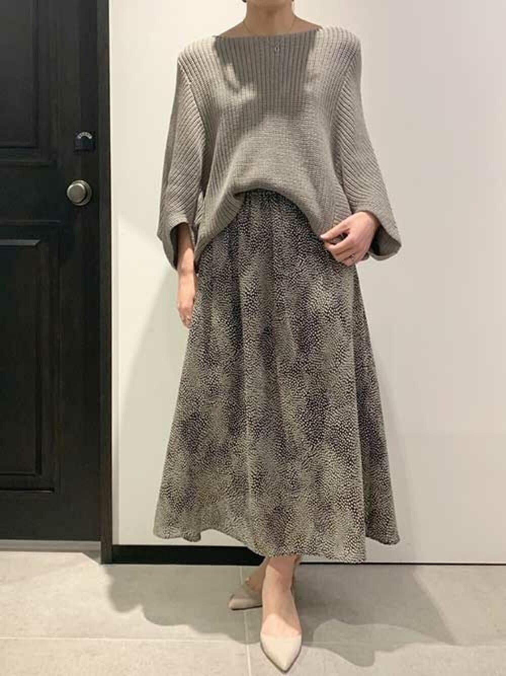 グレー系のパンプス、グレー系のニット/セーター、ブラック系のスカートを着用したレディースの春コーディネートの1枚目の写真