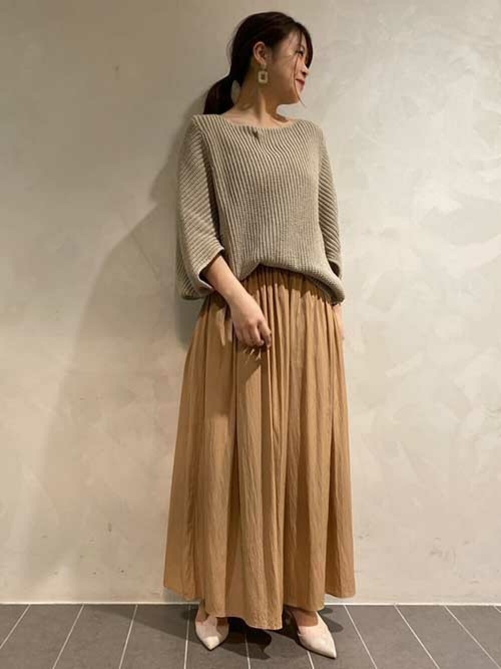 グレー系のパンプス、ベージュ系のスカート、ブラウン系のニット/セーターを着用したレディースの春コーディネートの1枚目の写真