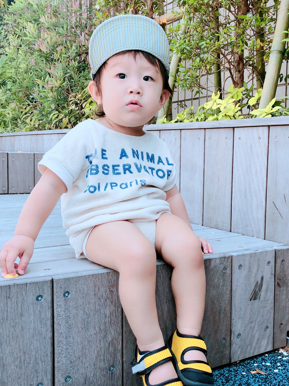 イエロー系のサンダル、ホワイト系のロンパース、ホワイト系のキャップを着用したキッズの夏コーディネートの1枚目の写真