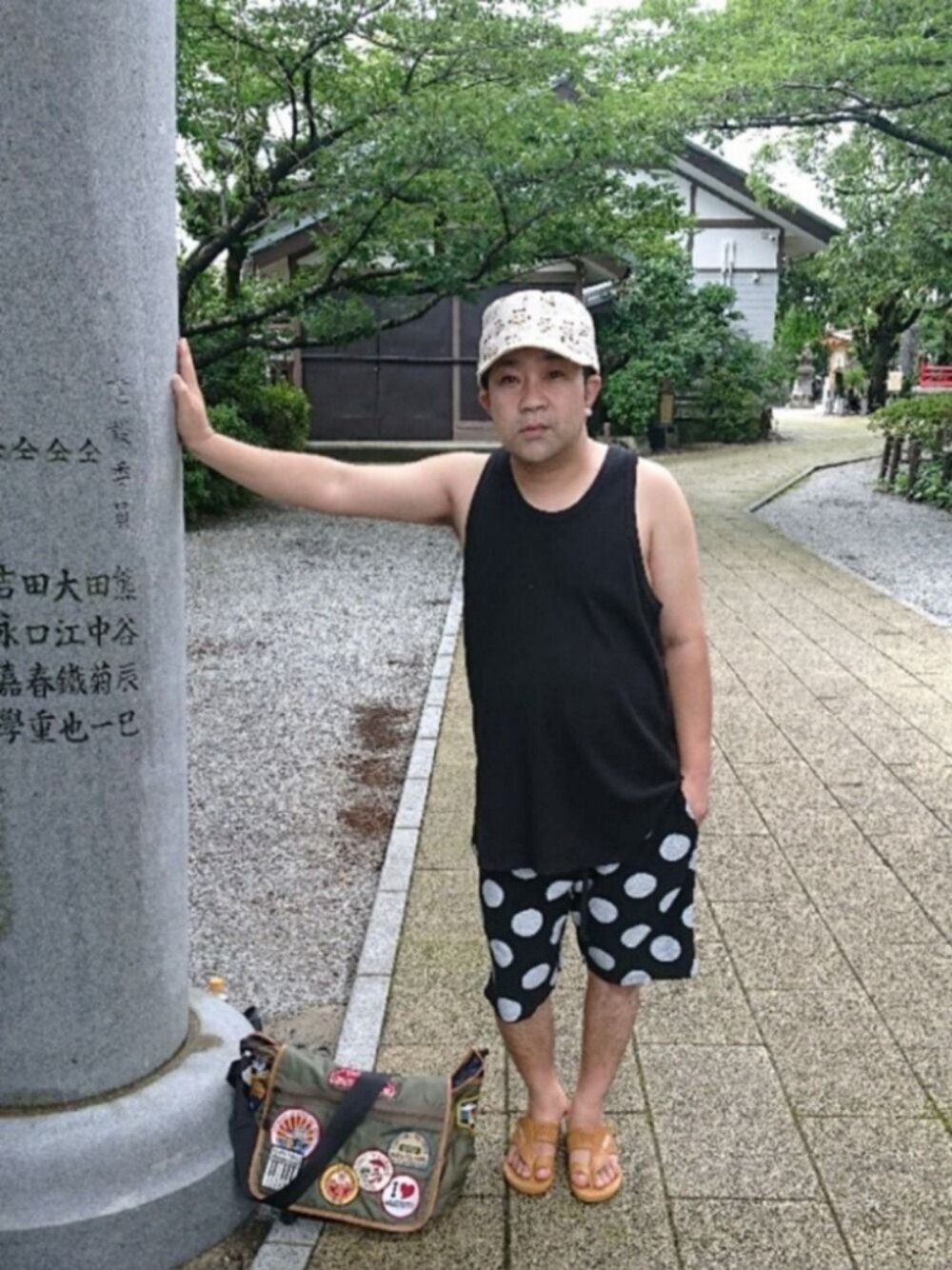 グリーン系のショルダーバッグ、ブラウン系のサンダル、ブラック系のパンツを着用したメンズの夏コーディネートの1枚目の写真