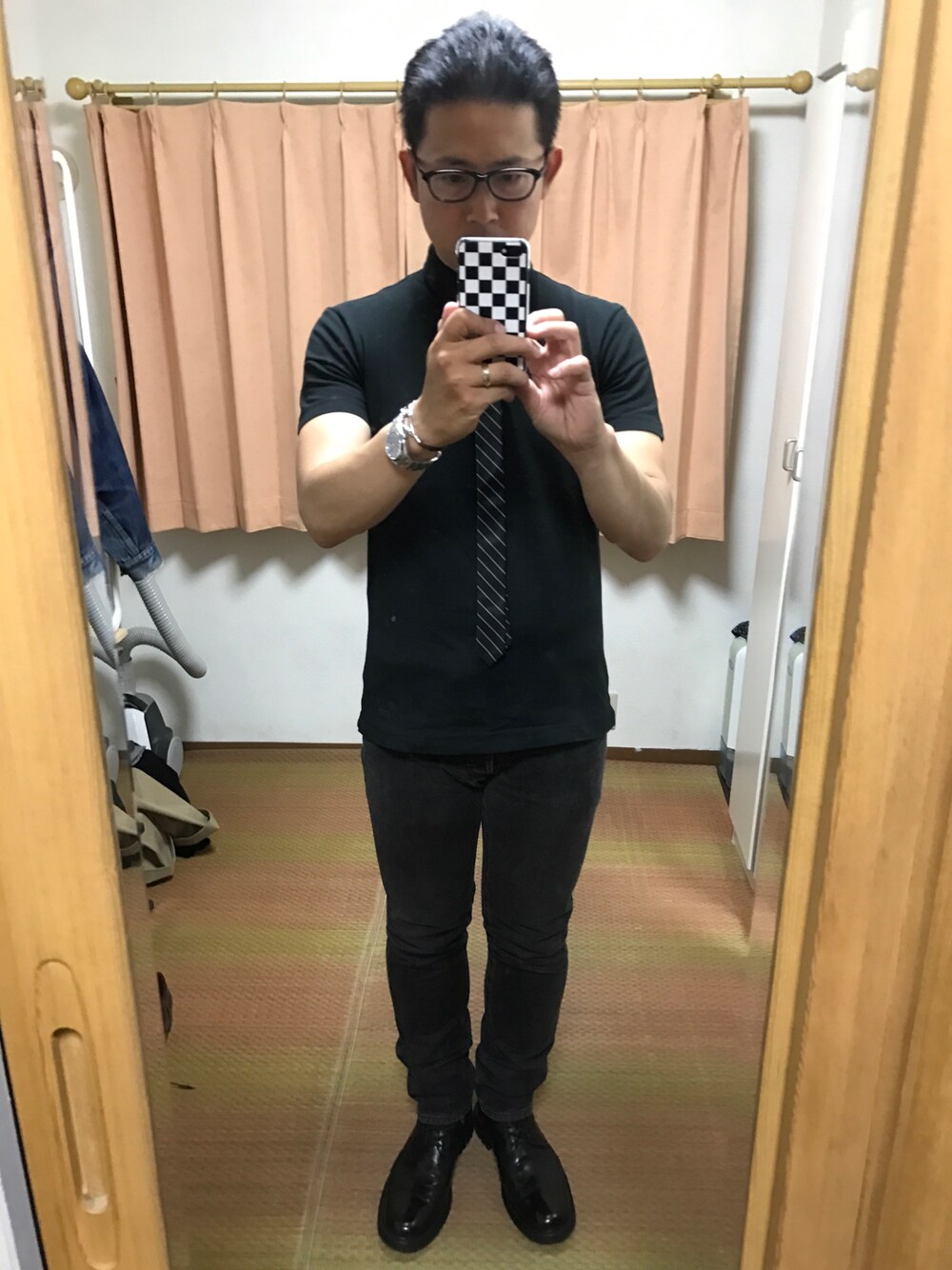 ブラック系のポロシャツ、ブラック系のネクタイ、ブラック系のデニムパンツを着用したメンズの春コーディネートの1枚目の写真