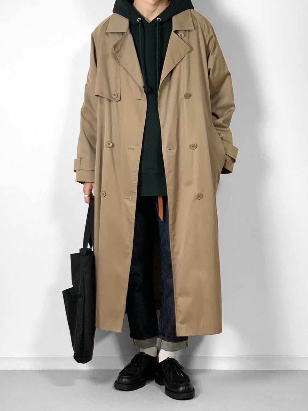 ベージュ系のトレンチコート、ブラック系のパーカー、ブルー系のデニムパンツを着用したメンズの秋コーディネートの1枚目の写真