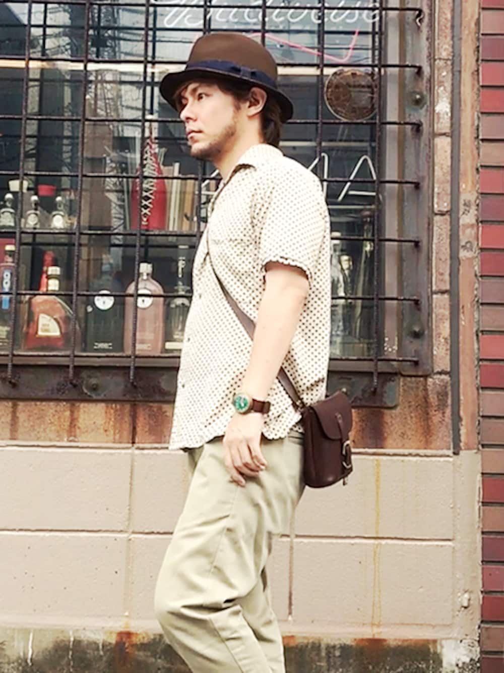 ブラウン系のショルダーバッグ、ブラウン系のハット、グリーン系のアナログ腕時計を着用したメンズの夏コーディネートの1枚目の写真