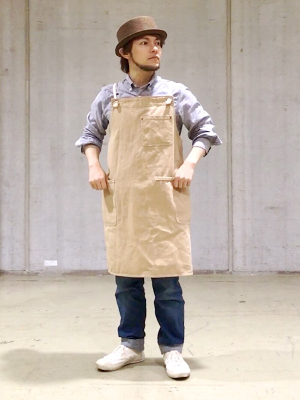 ブルー系のデニムパンツ、ホワイト系のスニーカー、ベージュ系のエプロンを着用したメンズの春コーディネートの1枚目の写真