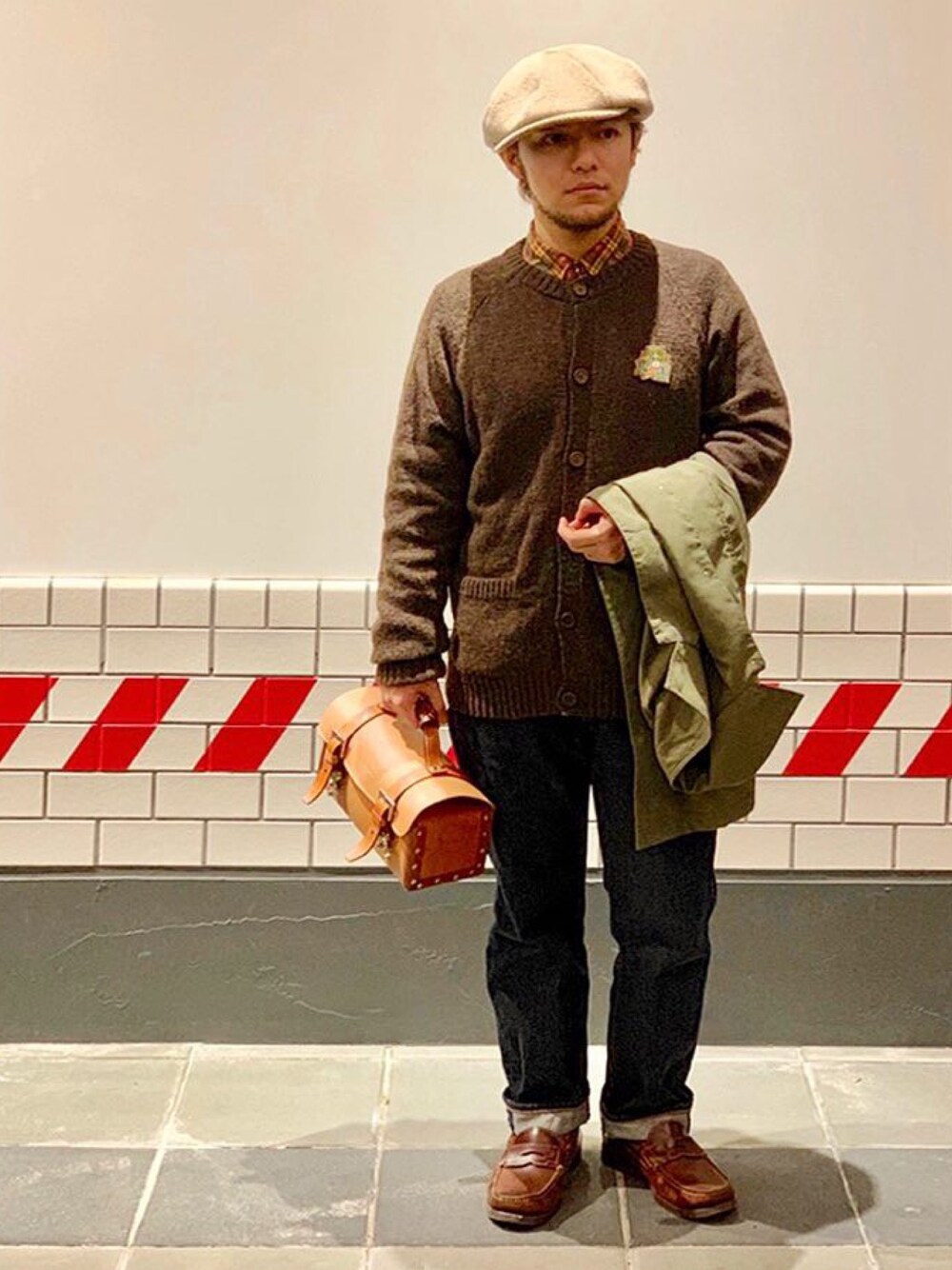 ブラウン系のカーディガン/ボレロ、グリーン系のステンカラーコート、ブルー系のデニムパンツを着用したメンズの冬コーディネートの1枚目の写真