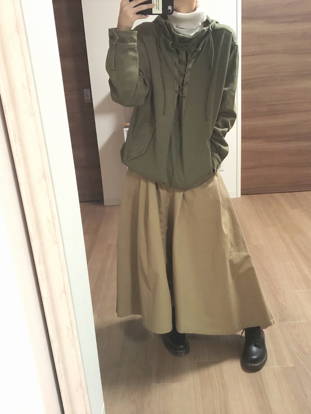 グリーン系のパーカー、ベージュ系のスカート、ブラック系のブーツを着用したレディースの冬コーディネートの1枚目の写真