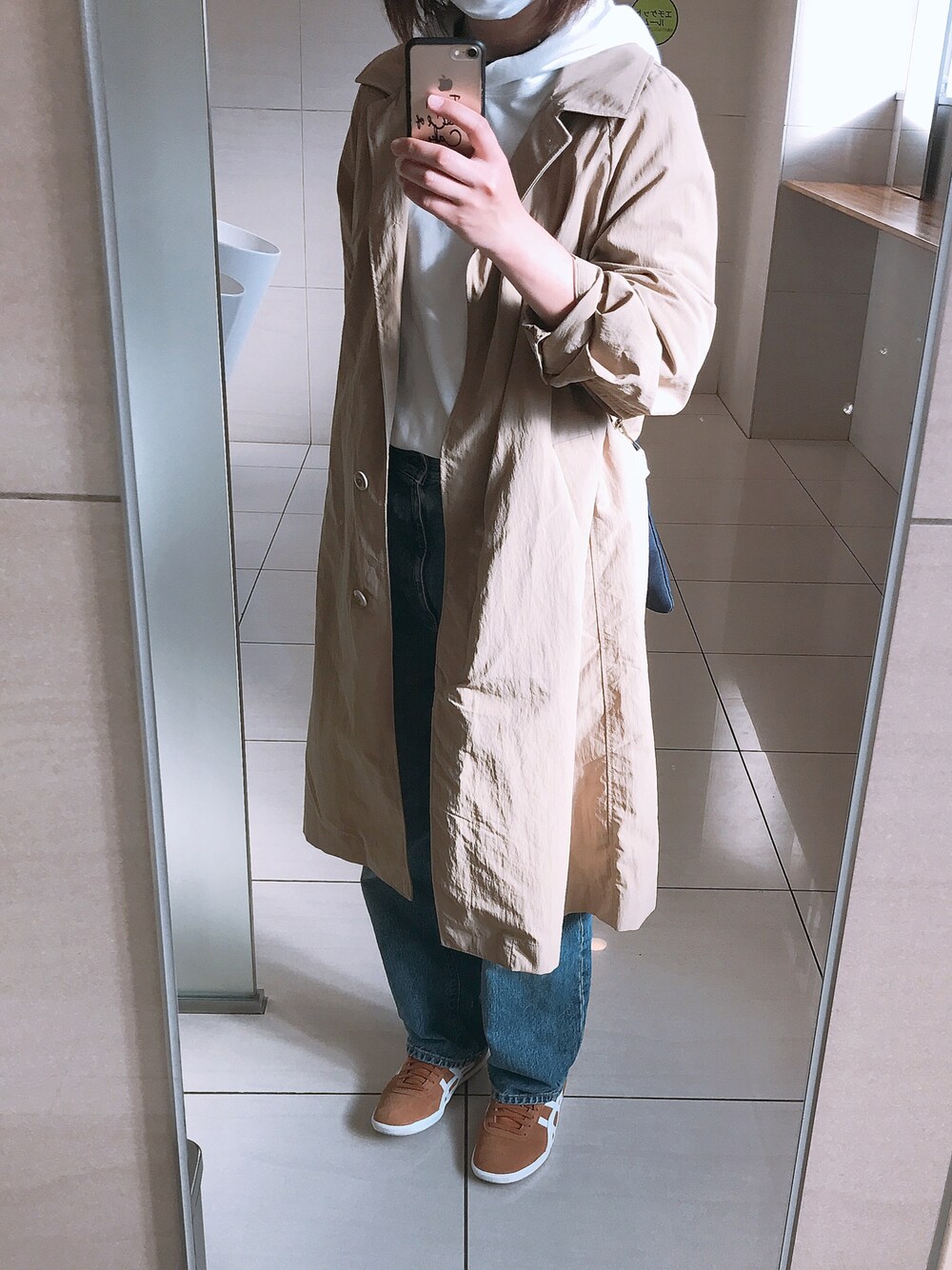 ベージュ系のステンカラーコート、ホワイト系のパーカー、ブルー系のデニムパンツを着用したレディースの春コーディネートの1枚目の写真