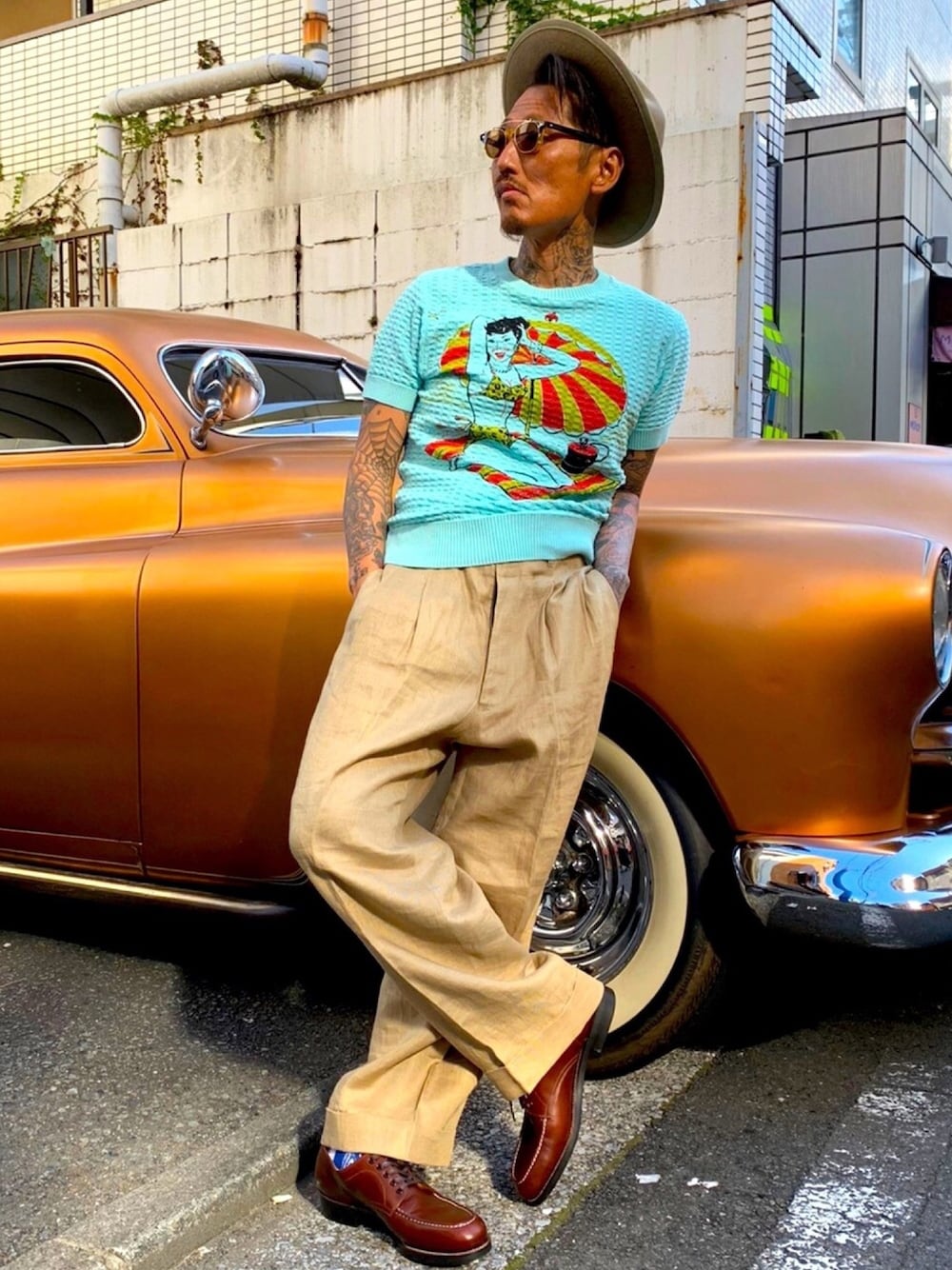 グレー系のニット/セーター、ベージュ系のスラックス、グリーン系のハットを着用したメンズの春コーディネートの1枚目の写真