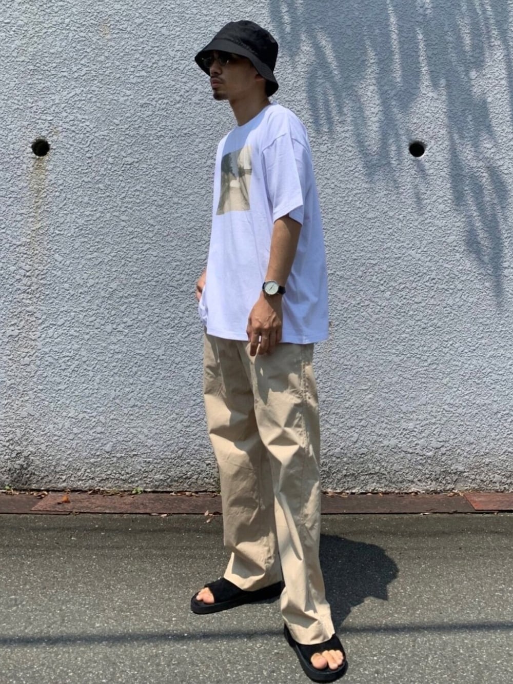 ホワイト系のTシャツ/カットソー、ブラック系のサンダル、ベージュ系のチノパンツを着用したメンズの夏コーディネートの1枚目の写真