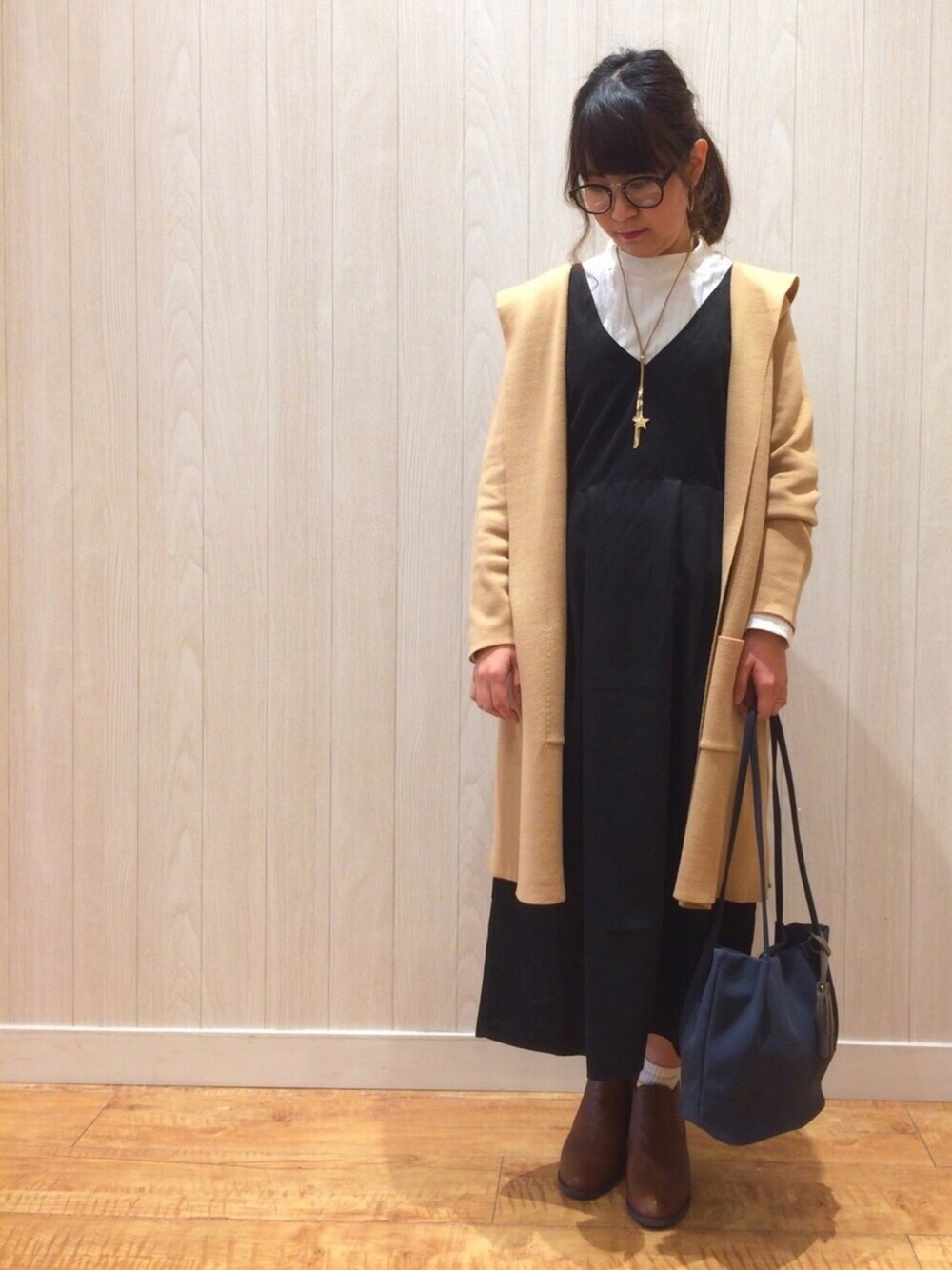 ブラック系のワンピース、ベージュ系のカーディガン/ボレロ、ブラウン系のブーツを着用したレディースの冬コーディネートの1枚目の写真