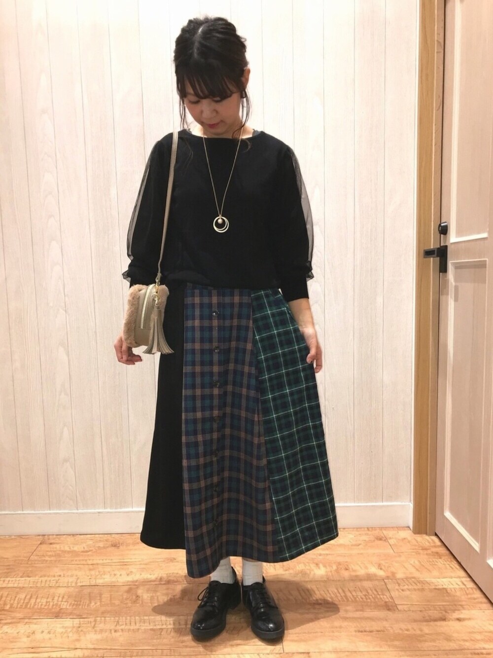 ベージュ系のショルダーバッグ、ブラック系のニット/セーター、グリーン系のスカートを着用したレディースの秋コーディネートの1枚目の写真