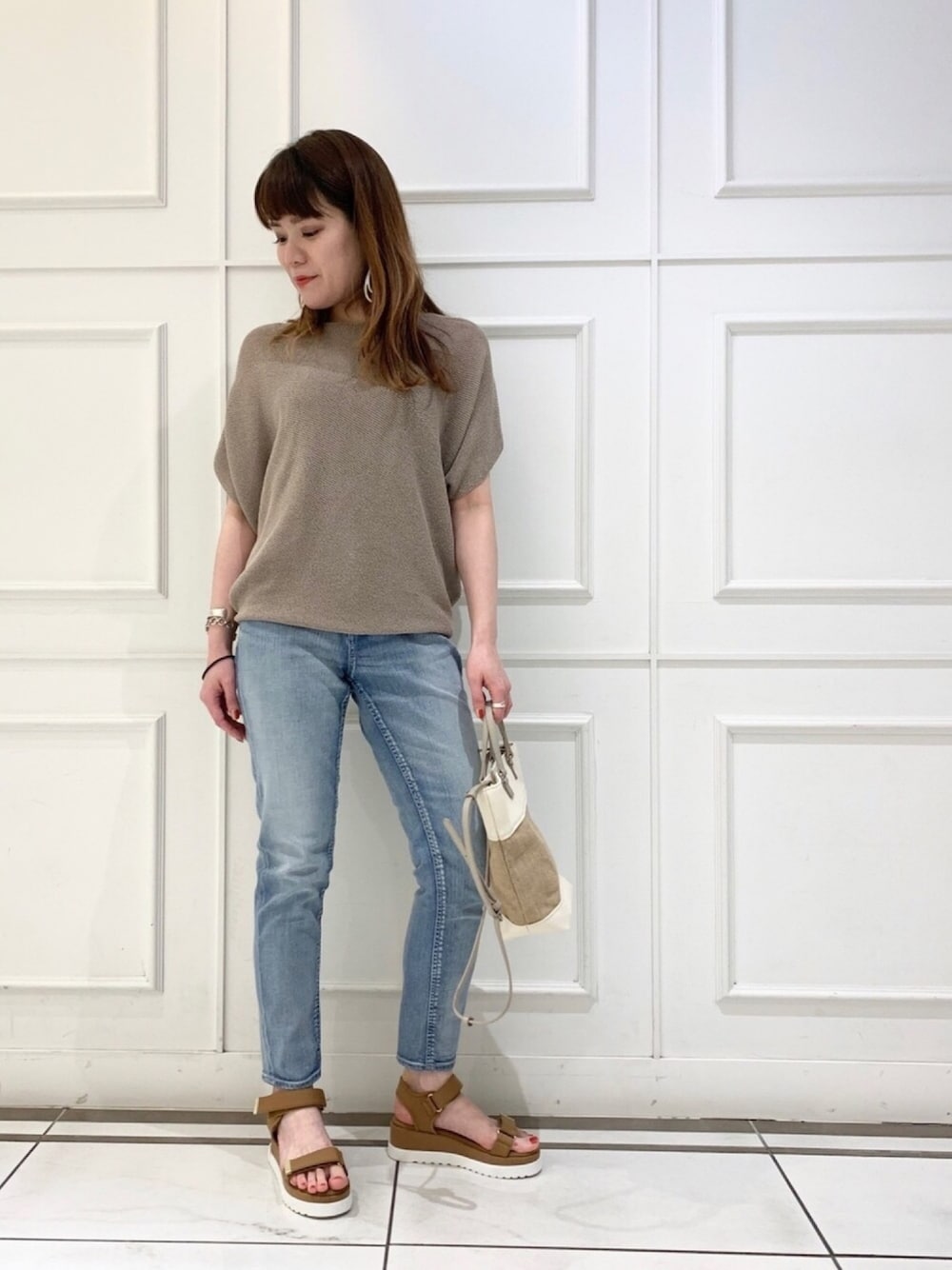 ベージュ系のニット/セーター、ブルー系のデニムパンツ、イエロー系のサンダルを着用したレディースの春コーディネートの1枚目の写真