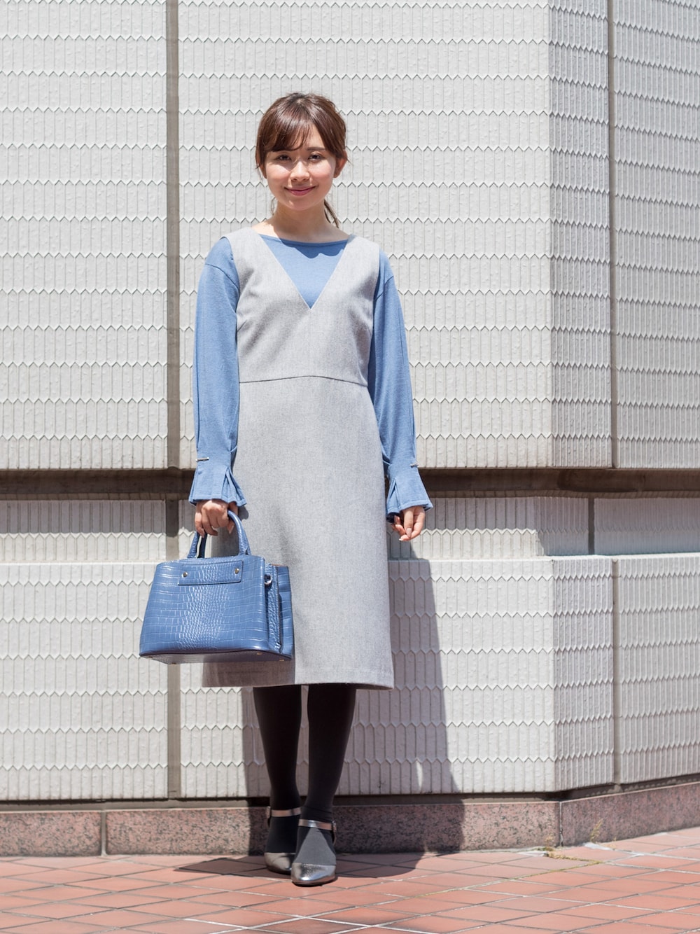 グレー系のジャンパースカート、ブルー系のトートバッグ、その他のパンプスを着用したレディースの秋コーディネートの1枚目の写真