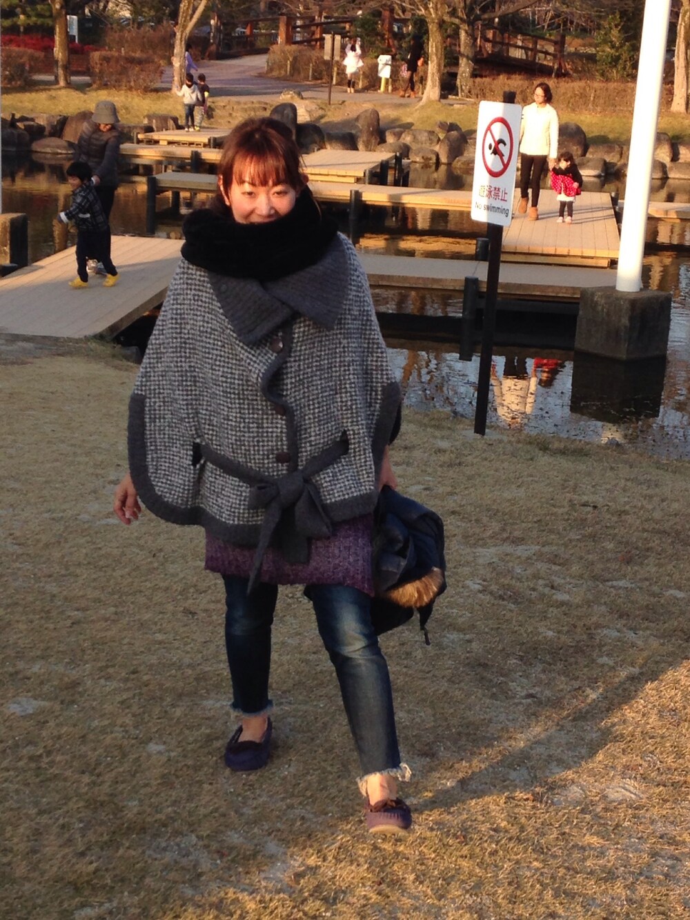 グレー系のポンチョ、パープル系のニット/セーター、ブルー系のデニムパンツを着用したレディースの冬コーディネートの1枚目の写真