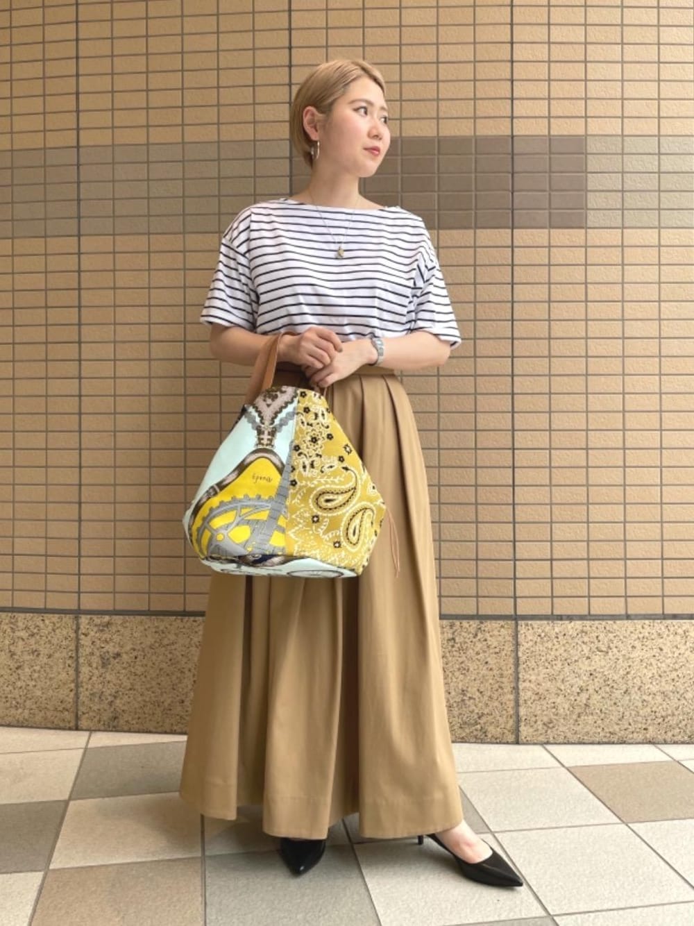 ベージュ系のスカート、ブラック系のTシャツ/カットソー、イエロー系のトートバッグを着用したレディースの夏コーディネートの1枚目の写真