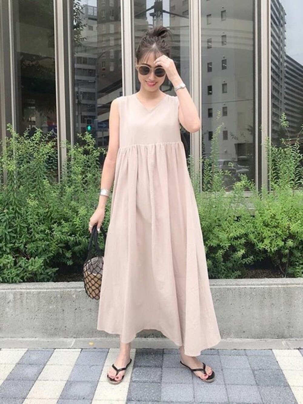 ベージュ系のワンピース、ブラック系のサンダル、ブラック系のかごバッグを着用したレディースの夏コーディネートの1枚目の写真