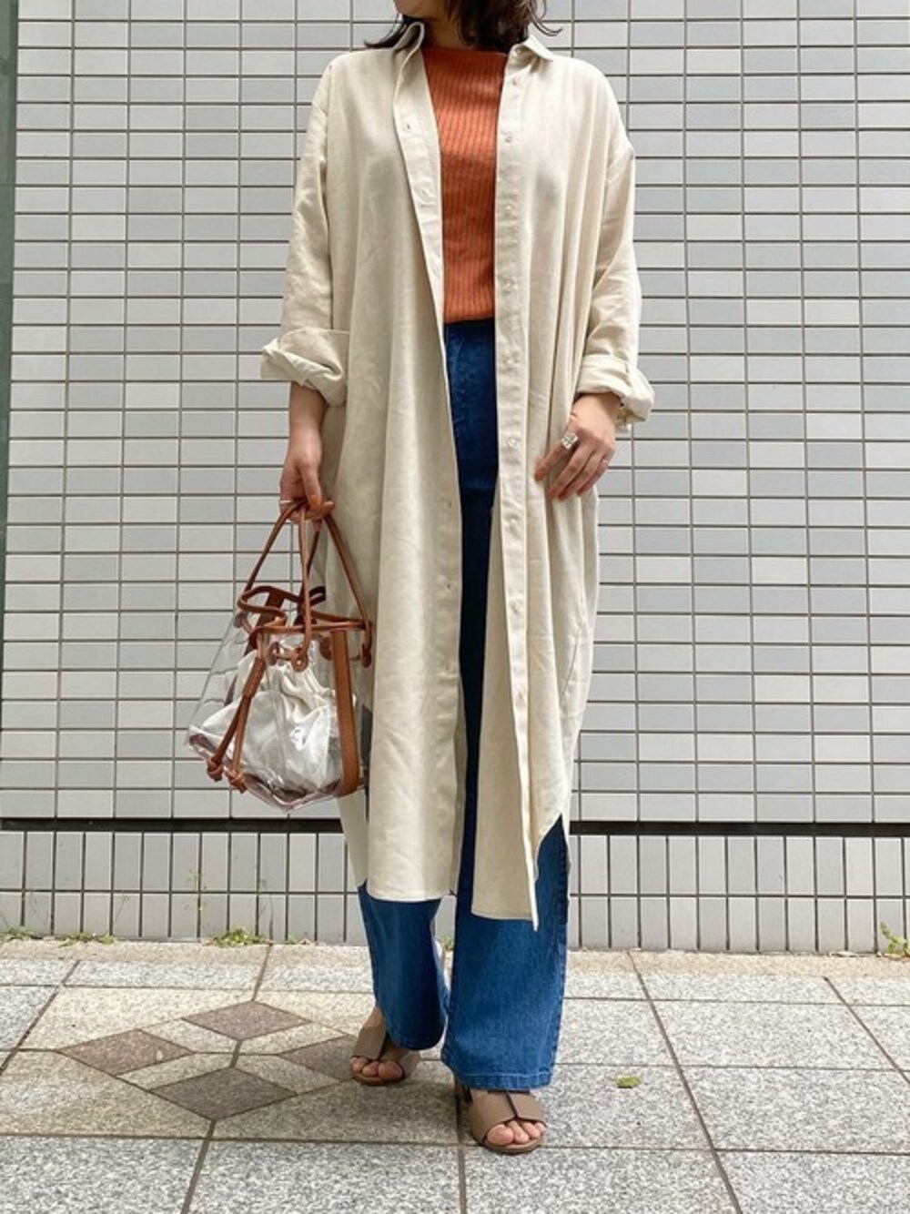 ベージュ系のシャツワンピース、オレンジ系のニット/セーター、ブルー系のデニムパンツを着用したレディースの夏コーディネートの1枚目の写真