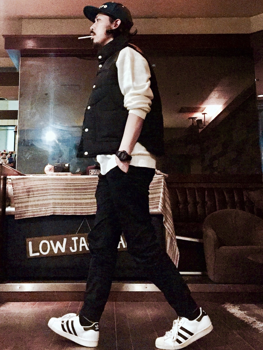 ブラック系のダウンベスト、ホワイト系のニット/セーター、ブラック系のチノパンツを着用したメンズの春コーディネートの1枚目の写真