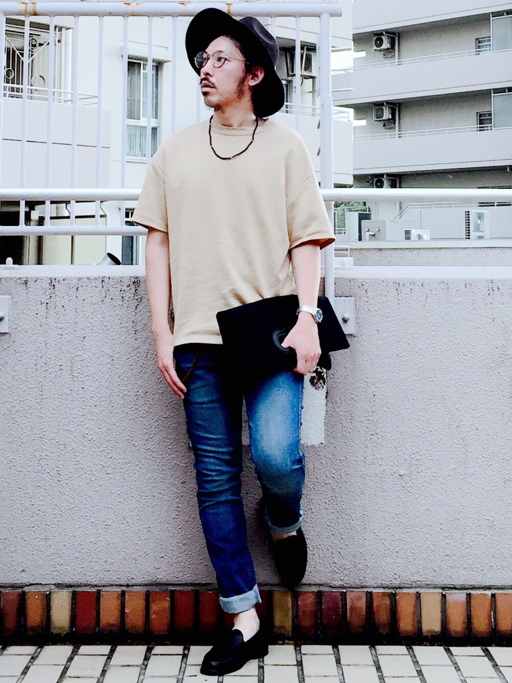 ベージュ系のTシャツ/カットソー、ブラック系のクラッチバッグ、ブルー系のデニムパンツを着用したメンズの春コーディネートの1枚目の写真