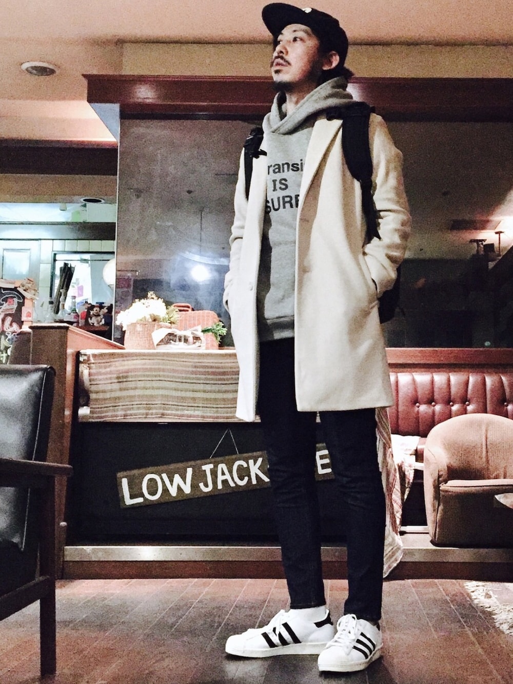 グレー系のパーカー、ホワイト系のチェスターコート、ブルー系のデニムパンツを着用したメンズの秋コーディネートの1枚目の写真