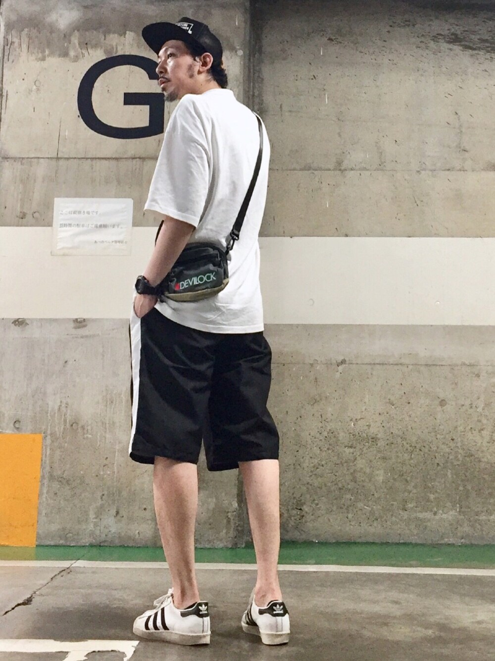 グレー系のショルダーバッグ、ホワイト系のスニーカー、ブラック系のキャップを着用したメンズの夏コーディネートの1枚目の写真