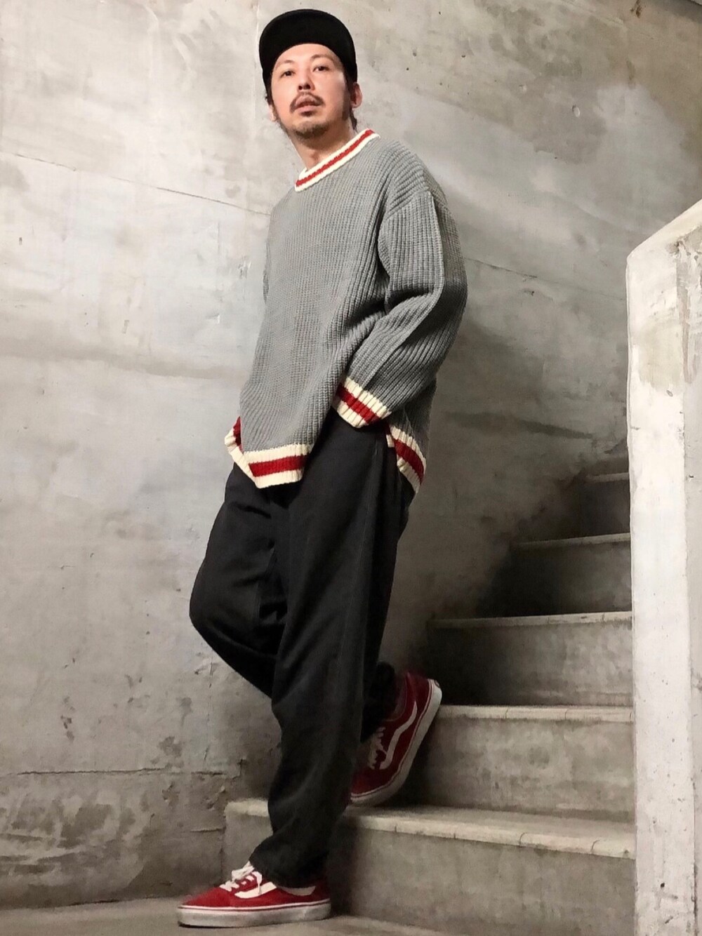 グレー系のニット/セーター、ブラック系のデニムパンツ、レッド系のスニーカーを着用したメンズの秋コーディネートの1枚目の写真