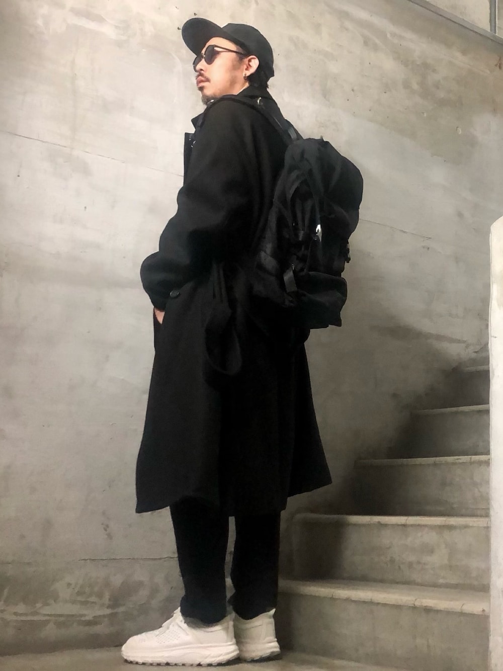 ブラック系のトレンチコート、ブラック系のスラックス、ブラック系のキャップを着用したメンズの冬コーディネートの1枚目の写真