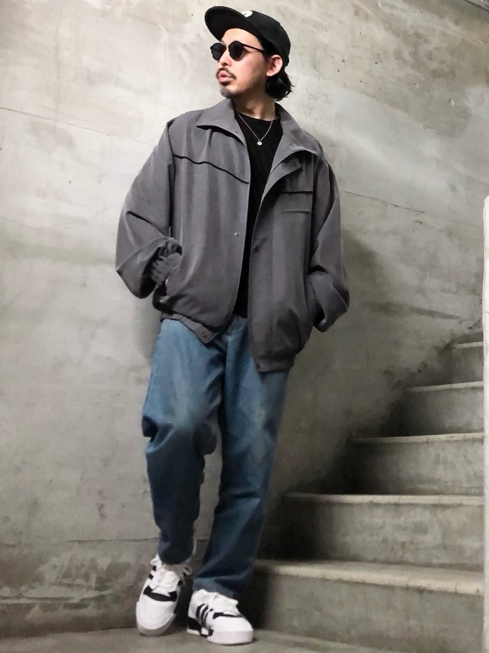グレー系のブルゾン、ホワイト系のスニーカー、ブルー系のデニムパンツを着用したメンズの春コーディネートの1枚目の写真