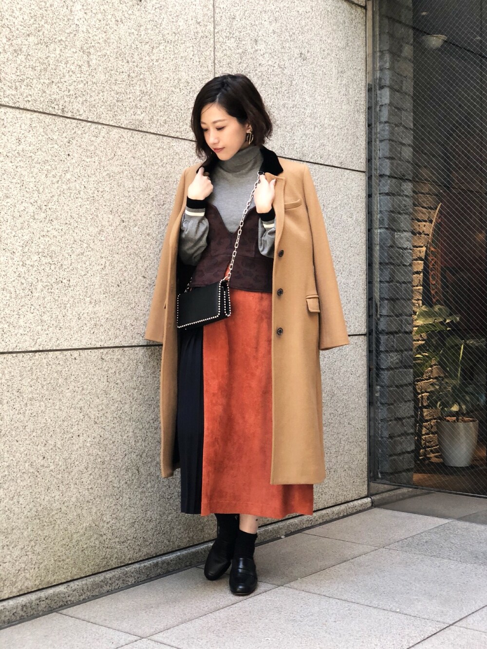 ベージュ系のチェスターコート、グレー系のニット/セーター、ブラウン系のスカートを着用したレディースの冬コーディネートの1枚目の写真