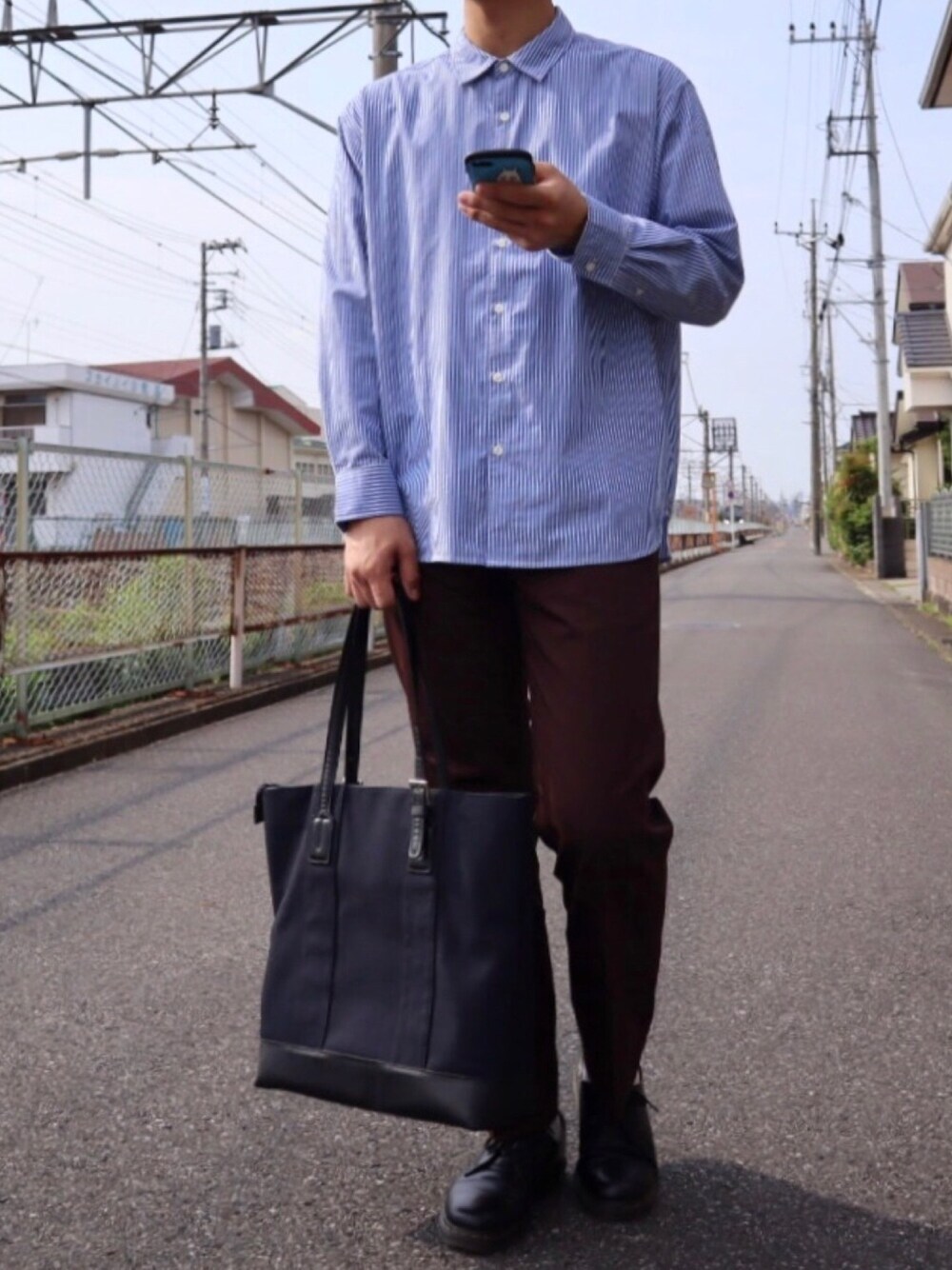 ブラック系のドレスシューズ、ブルー系のトートバッグ、レッド系のその他パンツを着用したメンズの春コーディネートの1枚目の写真