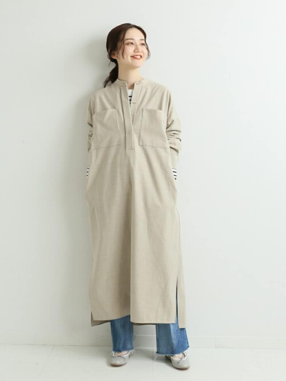 ベージュ系のシャツワンピース、ブルー系のデニムパンツを着用したレディースの冬コーディネートの1枚目の写真