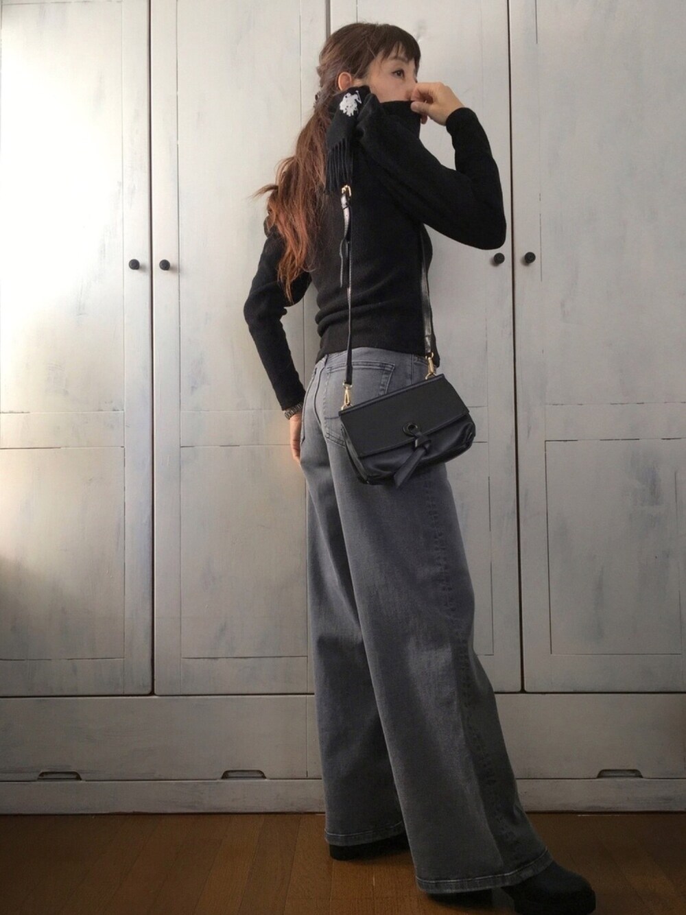 グレー系のデニムパンツ、ブラック系のブーツ、ブラック系のマフラーを着用したレディースの秋コーディネートの1枚目の写真