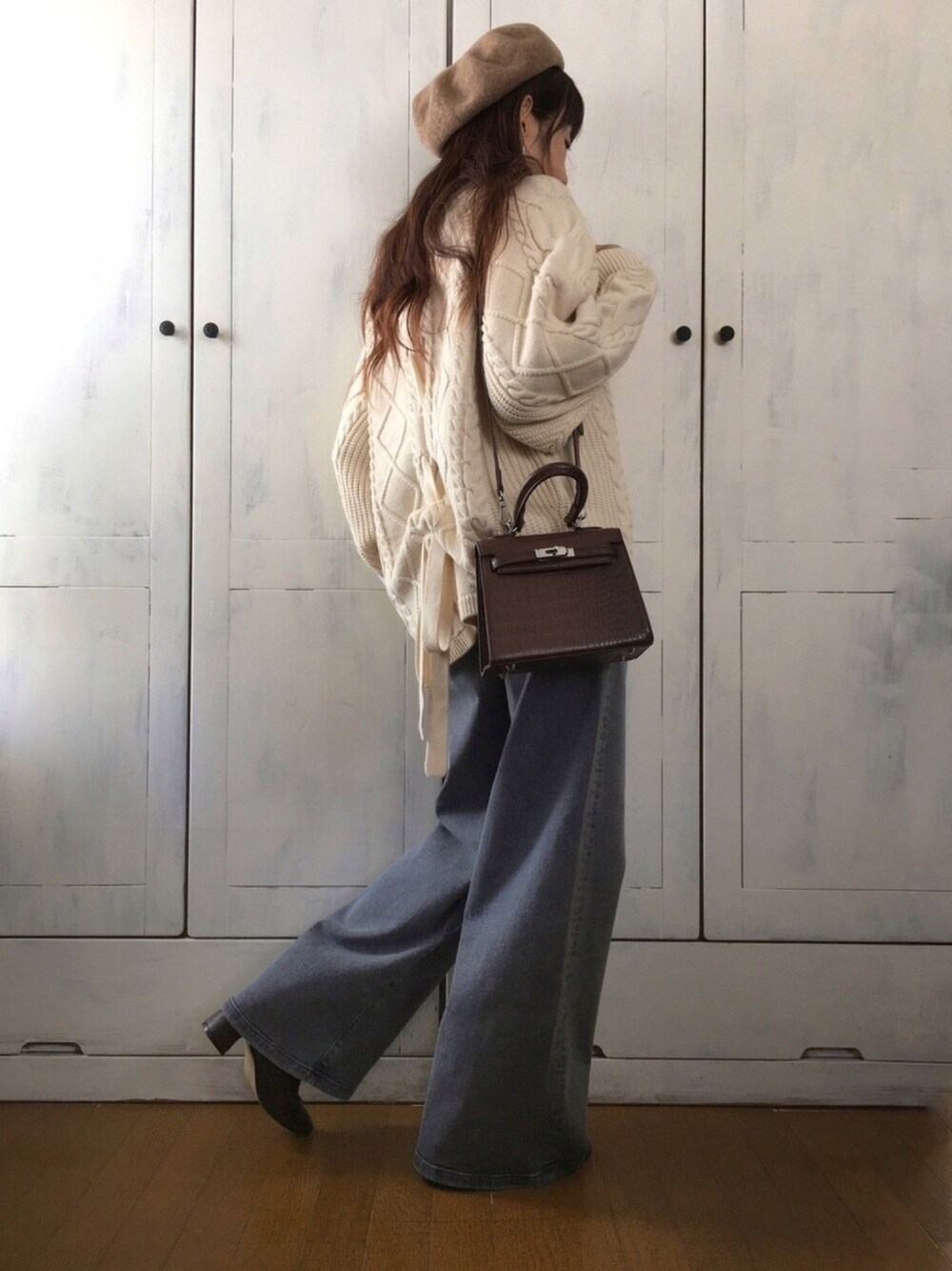 ホワイト系のニット/セーター、ブラウン系のハンドバッグ、グレー系のデニムパンツを着用したレディースの冬コーディネートの1枚目の写真
