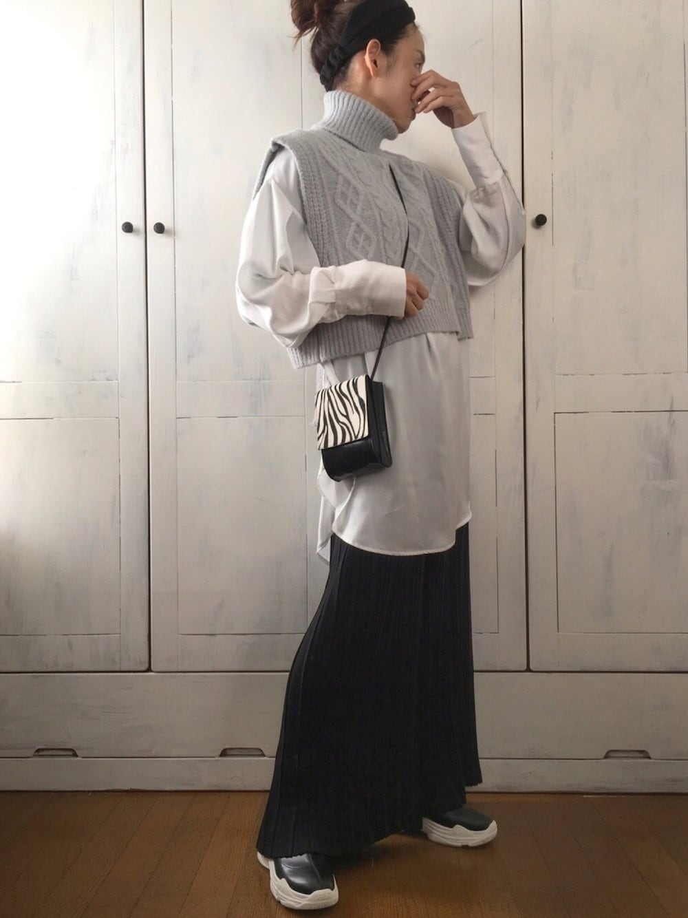 グレー系のニット/セーター、ホワイト系のシャツ/ブラウス、ブラック系のショルダーバッグを着用したレディースの冬コーディネートの1枚目の写真