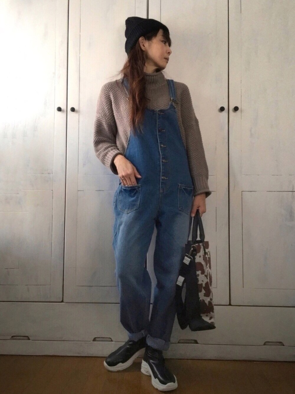 ブラウン系のニット/セーター、ブルー系のサロペット/オーバーオール、ブラウン系のトートバッグを着用したレディースの冬コーディネートの1枚目の写真