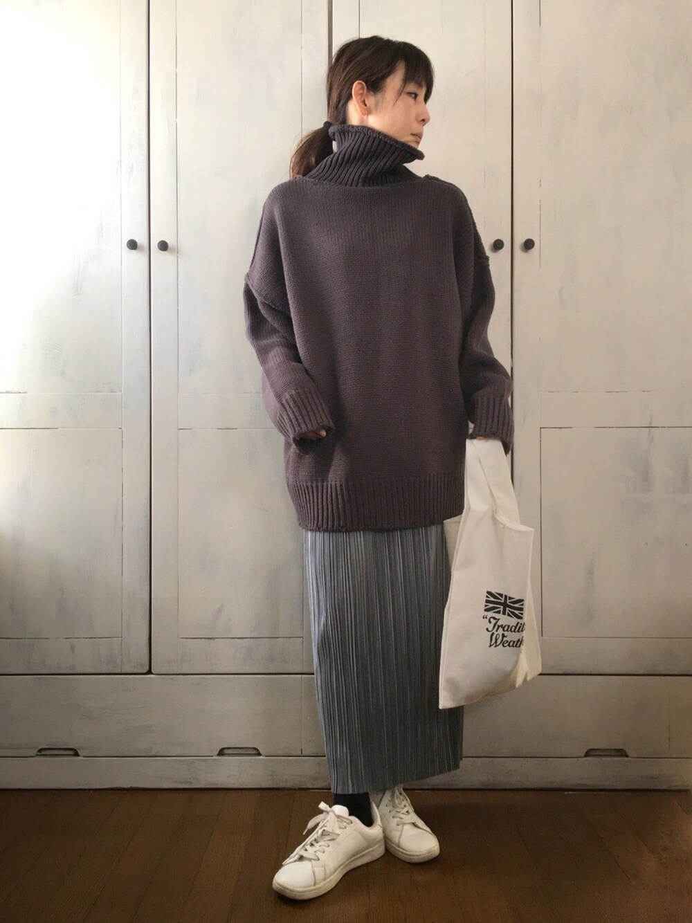 グレー系のニット/セーター、ブルー系のスカート、ホワイト系のエコバッグ/サブバッグを着用したレディースの冬コーディネートの1枚目の写真