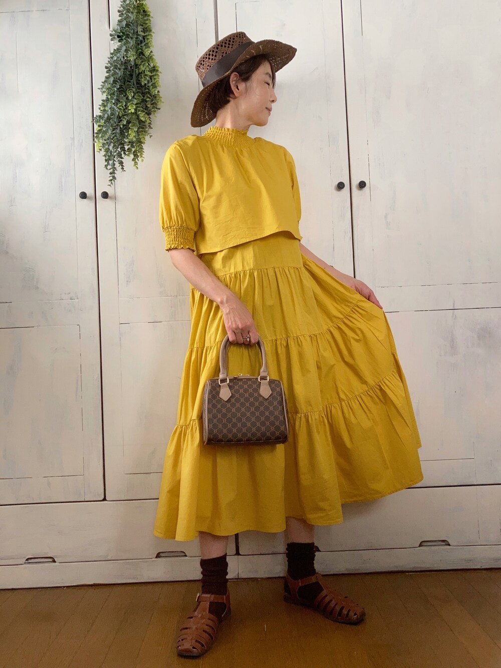 イエロー系のワンピース、ブラウン系のボストンバッグ、ブラウン系のサンダルを着用したレディースの夏コーディネートの1枚目の写真